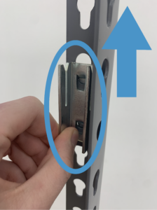 a hand holds a shelf clip with and is emphasized by being surrounded by a blue circle. Next to it a blue arrows signals that you must pull up to disengage the clip