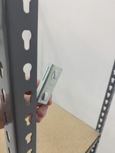 A hand holds a shelf clip that waas just pulled from the shelving unit